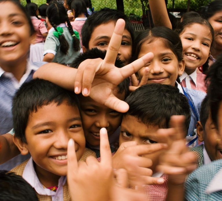 Group of smiling children posing and making hand gestures outdoors.